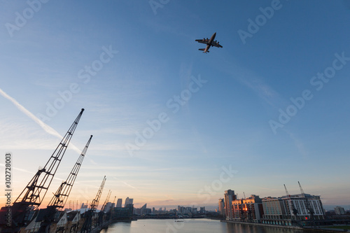 Passenger plane flying over the Thames River at sunset, Royal Victoria Dock, London, England photo