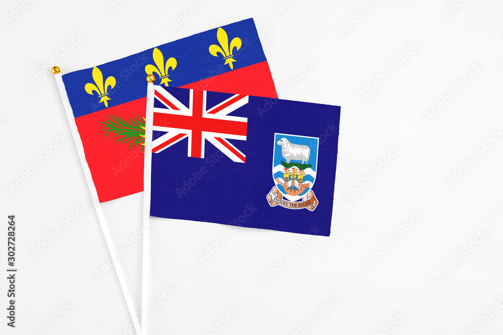 Fototapeta premium Falkland Islands and Guadeloupe stick flags on white background. High quality fabric, miniature national flag. Peaceful global concept.White floor for copy space.