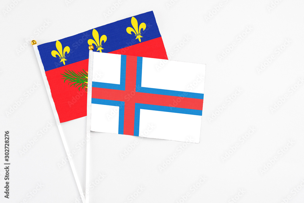 Faroe Islands and Guadeloupe stick flags on white background. High quality fabric, miniature national flag. Peaceful global concept.White floor for copy space.