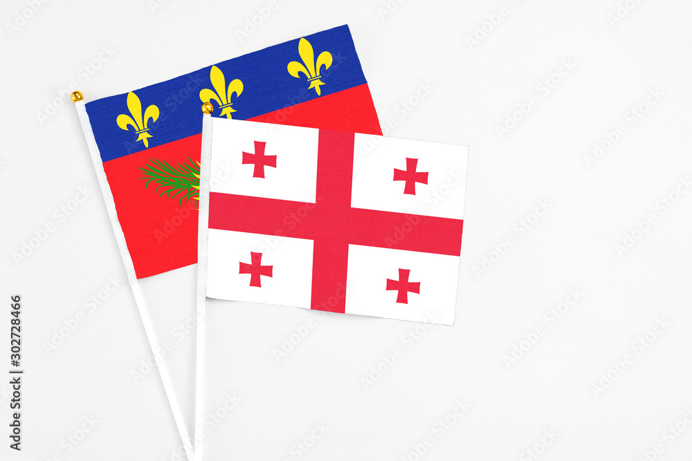 Georgia and Guadeloupe stick flags on white background. High quality fabric, miniature national flag. Peaceful global concept.White floor for copy space.