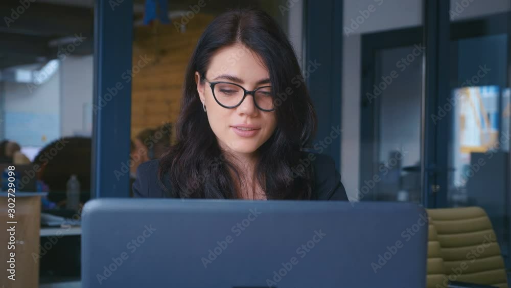 Attractive Young Businesswoman in Glasses Working on a Laptop in Modern Office Attractive Young Businesswoman in Glasses Working on a Laptop in Modern Office
