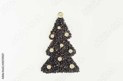 Christmas tree made from freshly roasted coffee beans and decorated small cups of cappuccino on white table. Winter concept. Creative. Minimalism