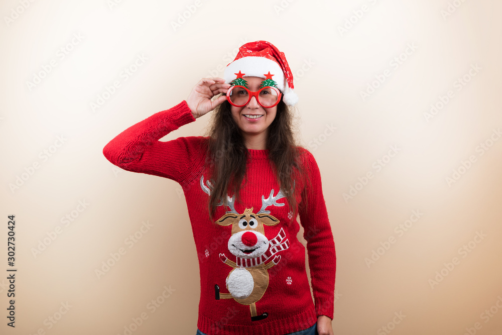 Young woman with dental braces in Christmas knitted sweater with reindeer, glasses and Santa's hat on beige background Young woman with dental braces in Christmas knitted sweater with reindeer, glasses and Santa's hat on beige background