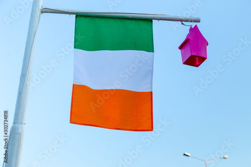 Flag of Ireland on a post with a small pink light in form of a birdhouse. Real photo of a weaving flag.