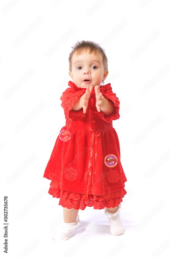 Enthusiastic baby girl in red child dress and white socks standing and catching soap bubbles. Light background Enthusiastic baby girl in red child dress and white socks standing and catching soap bubbles. Light background