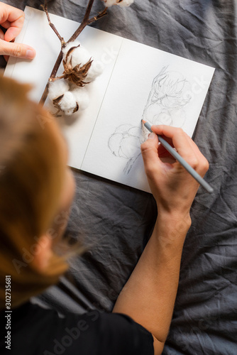 Girl draws a pencil sketch of cotton in a sketchbook. Hobbies and leisure. 