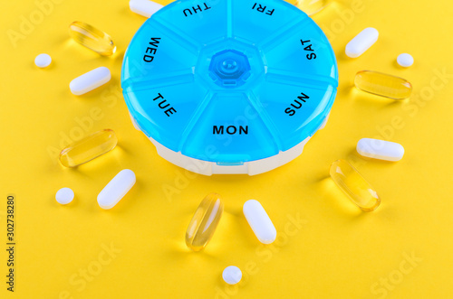 different medicines for one week and a pills box on yellow background photo
