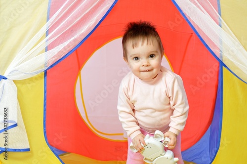 Little cute baby girl holds toy on hands in little house. Playful toddler portrait. Happy childhood