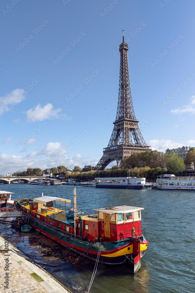 Naklejka premium Eiffel tower across Seine River, in foreground are parked boats