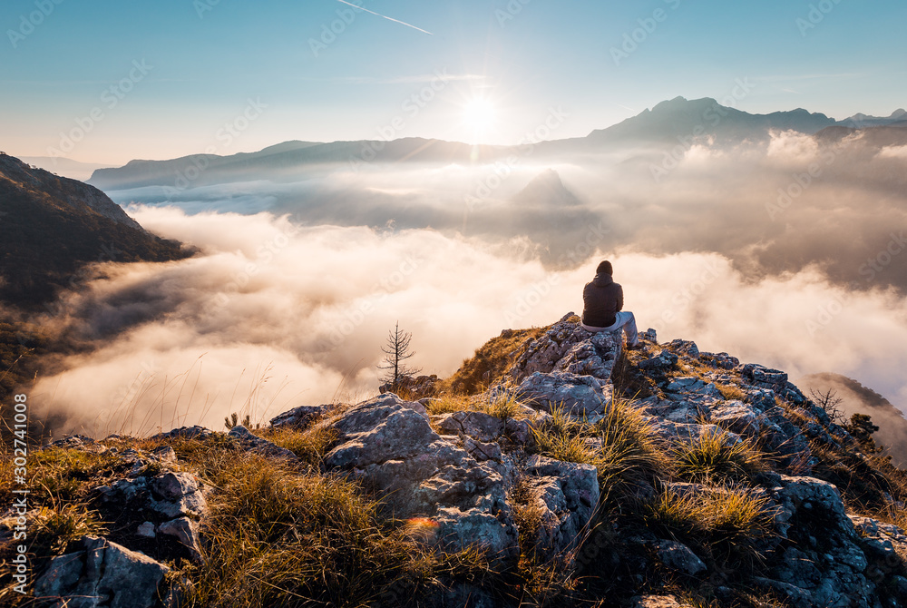 Man sitting an top of mountain at sunrise and enjoying the view - obrazy, fototapety, plakaty 
