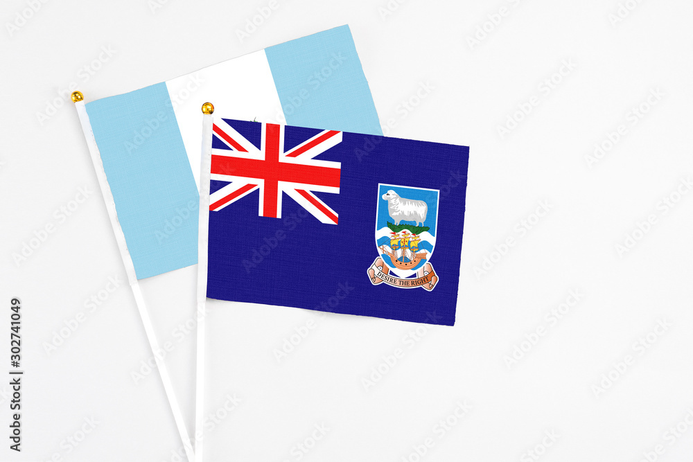 Fototapeta premium Falkland Islands and Guatemala stick flags on white background. High quality fabric, miniature national flag. Peaceful global concept.White floor for copy space.