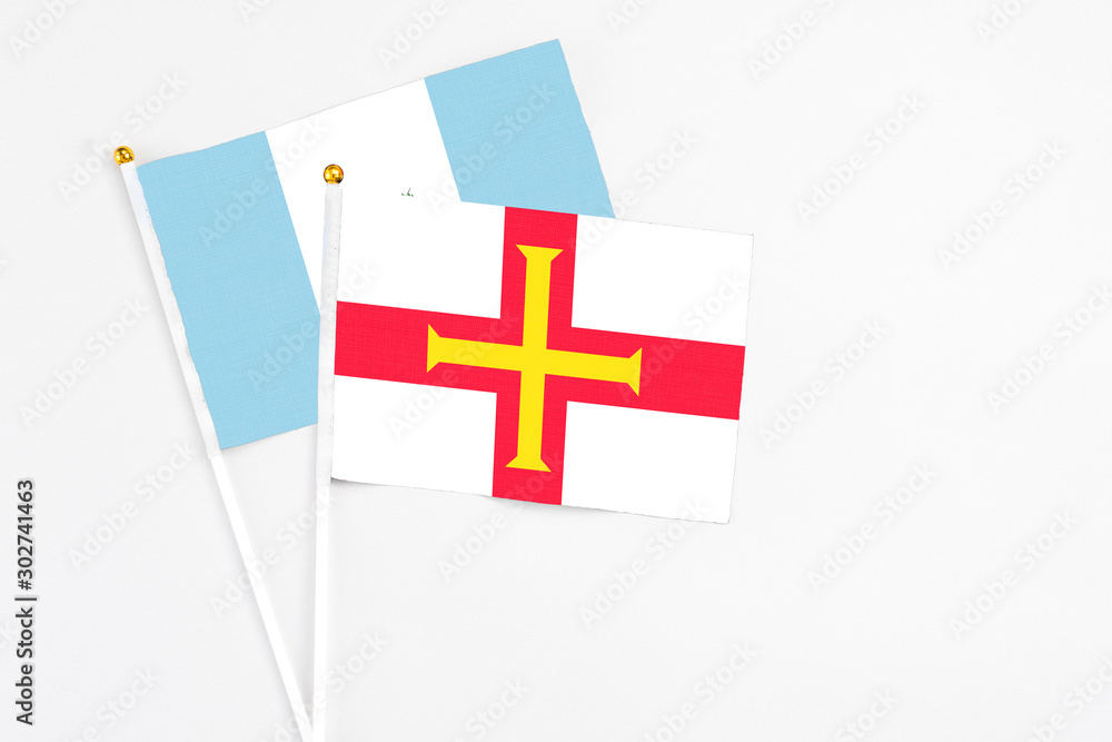 Guernsey and Guatemala stick flags on white background. High quality fabric, miniature national flag. Peaceful global concept.White floor for copy space.