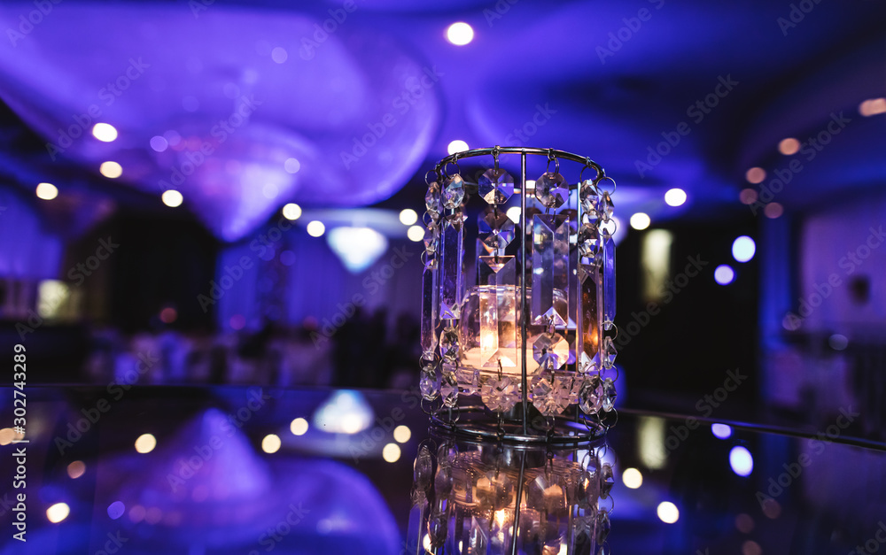 Glass candle light on background of the purple events room. Crystal glass lights indoor of party hall. Beautiful violet decoration in modern banquet restaurant. Holiday table setting.