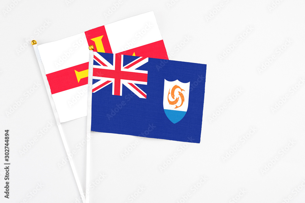 Fototapeta premium Anguilla and Guernsey stick flags on white background. High quality fabric, miniature national flag. Peaceful global concept.White floor for copy space.