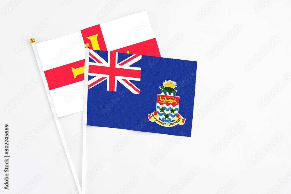 Fototapeta premium Cayman Islands and Guernsey stick flags on white background. High quality fabric, miniature national flag. Peaceful global concept.White floor for copy space.