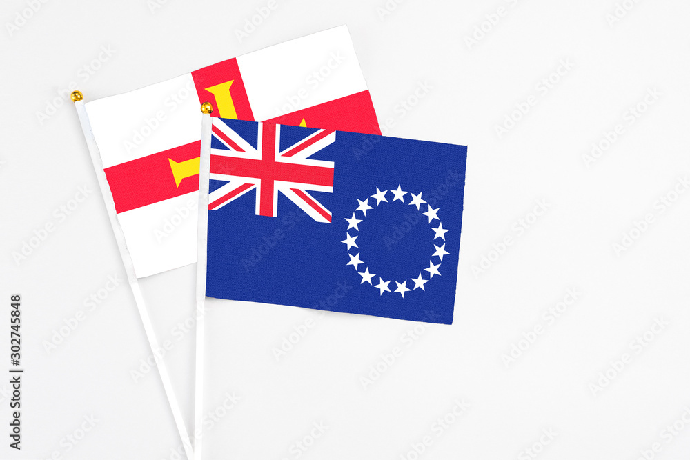 Cook Islands and Guernsey stick flags on white background. High quality fabric, miniature national flag. Peaceful global concept.White floor for copy space.
