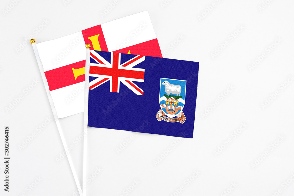 Fototapeta premium Falkland Islands and Guernsey stick flags on white background. High quality fabric, miniature national flag. Peaceful global concept.White floor for copy space.