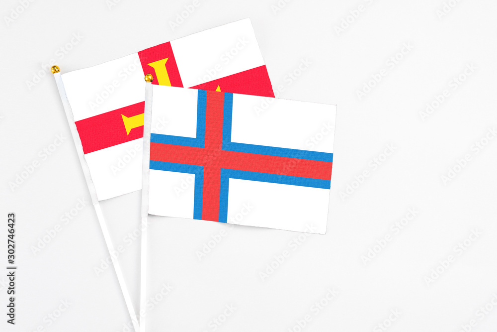 Faroe Islands and Guernsey stick flags on white background. High quality fabric, miniature national flag. Peaceful global concept.White floor for copy space.