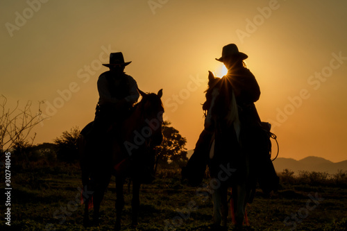 silhouette of cowboys on horseback at sunset © AUNTYANN