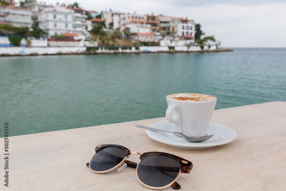 Cup of cappuccino in a cafe terrace on wooden table with blurred landscape on the background. Cup of cappuccino in a cafe terrace on wooden table with blurred landscape on the background.