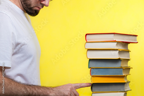 Concept of education. A man in a white t-shirt points to the penultimate book in the pile. Yellow background