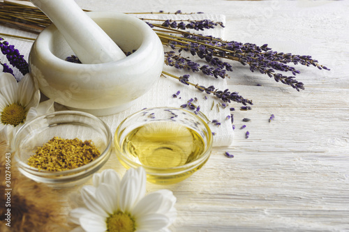 Composition with dried lavender flowers in white marble pestle and mortar and natural chamomile oil cosmetic in glass jar on white background, top view with free copy space