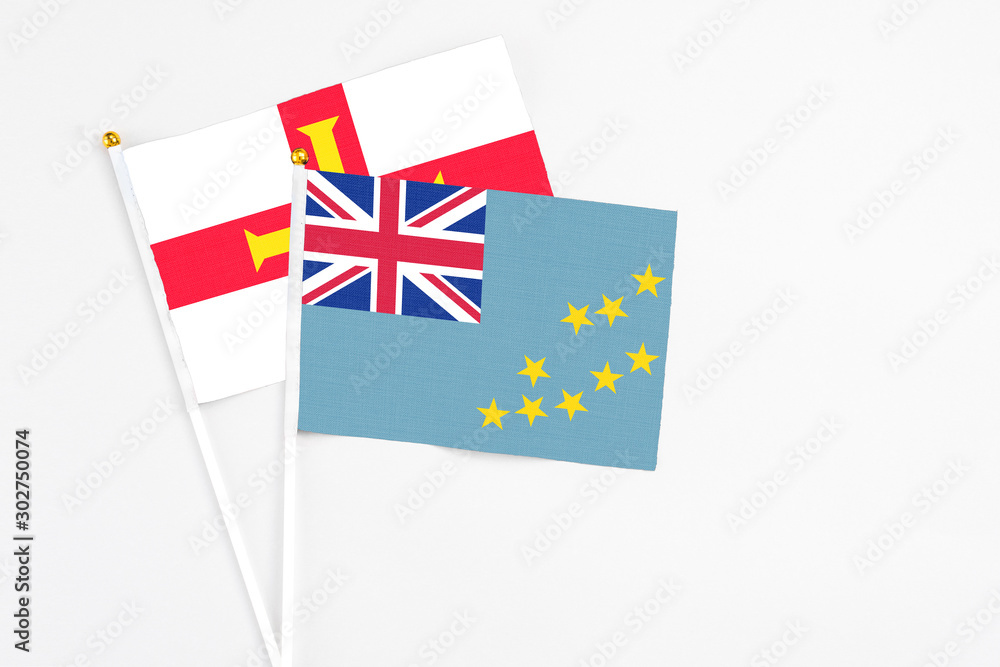Fototapeta premium Tuvalu and Guernsey stick flags on white background. High quality fabric, miniature national flag. Peaceful global concept.White floor for copy space.