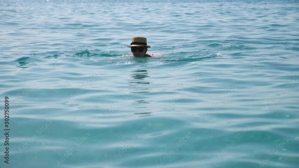 Young woman swimming in open sea enjoying summer vacation or holiday. Girl in hat relaxing on exotic resort floating in azure clear water. Concept of travel or summer vacation. Slow motion Close up Young woman swimming in open sea enjoying summer vacation or holiday. Girl in hat relaxing on exotic resort floating in azure clear water. Concept of travel or summer vacation. Slow motion Close up