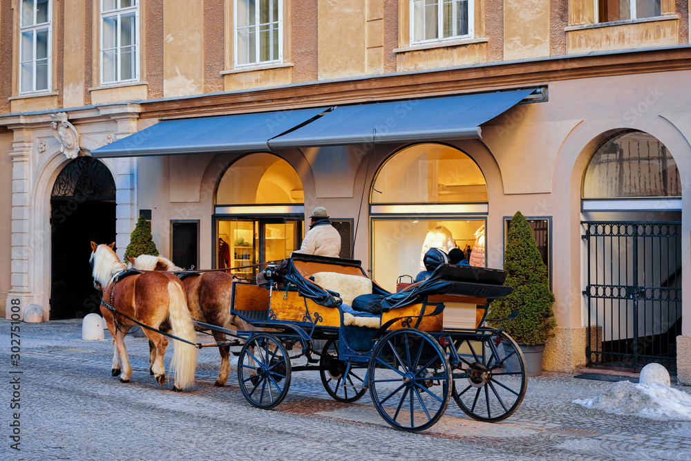Horse fiaker on street with snow in Salzburg of Austria. Mozart city in Europe at winter. Carriage fiacre transport. Panoramic view and cityscape of beautiful old Austrian town of Salzburgerland.