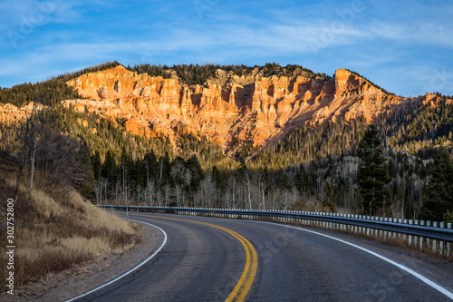 State Road 14 leads toward cliff of orange and red rock towers and hoodoos.
