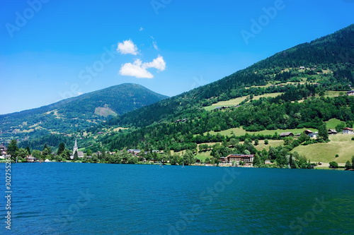 Panorama of lake Field am See in Carinthia in Austria. Landscape with pond and blue sky in spring or summer. Scenery in green Alps of Europe. Countryside with Alpine mountains. Nature with water
