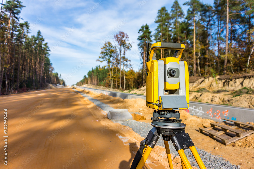 Surveyors equipment (theodolite or total positioning station) on the construction site of the road or building with construction machinery background Surveyors equipment (theodolite or total positioning station) on the construction site of the road or building with construction machinery background