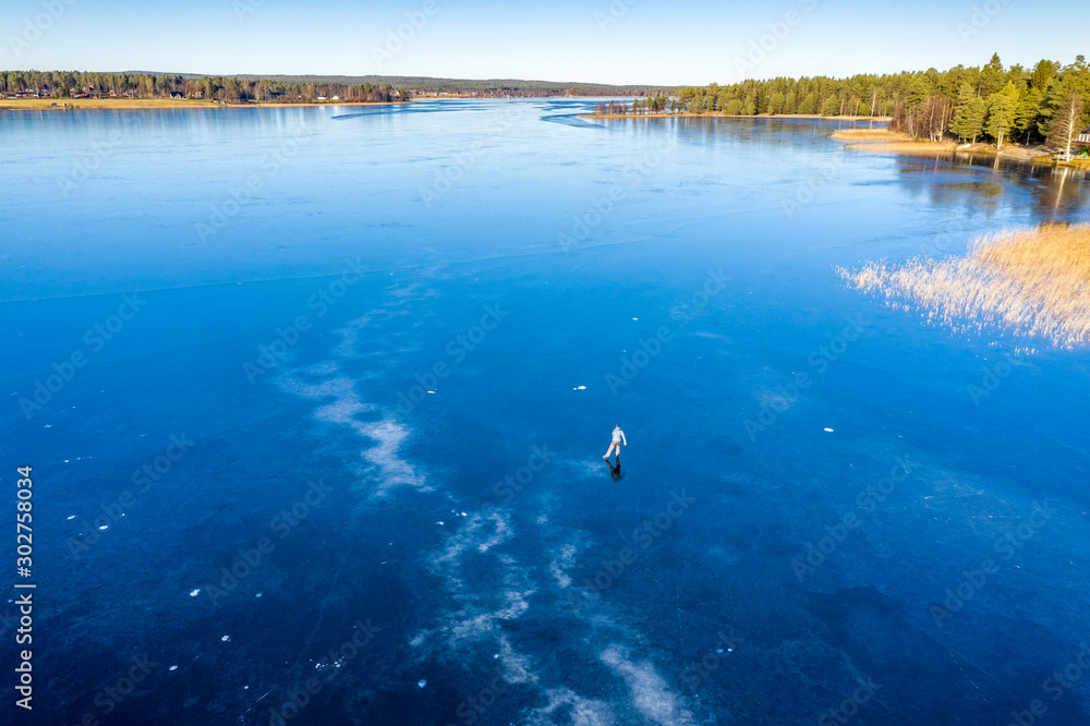 Aerial scenic view: unidentified person ice skating on crystal clear frozen lake in Northern Scandianvia. Clear skies, blue ice, winter day. Frozen lake like mirror, Lappland, Sweden Aerial scenic view: unidentified person ice skating on crystal clear frozen lake in Northern Scandianvia. Clear skies, blue ice, winter day. Frozen lake like mirror, Lappland, Sweden