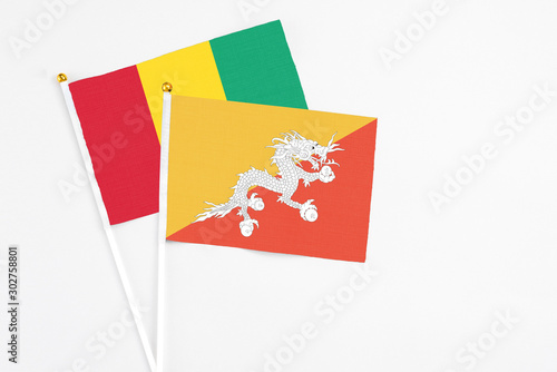 Bhutan and Guinea stick flags on white background. High quality fabric, miniature national flag. Peaceful global concept.White floor for copy space.