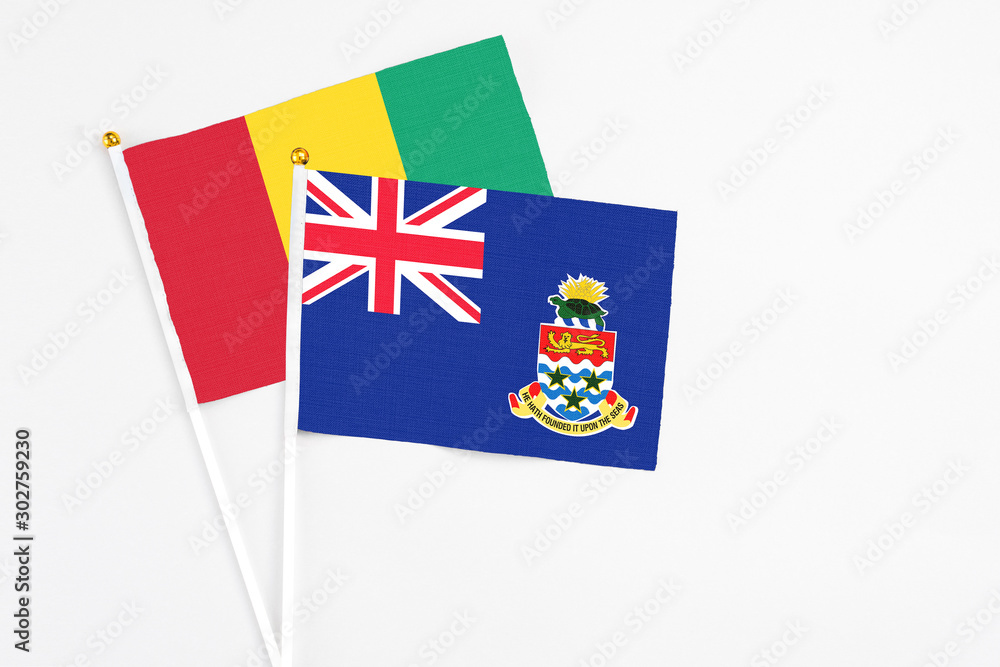 Fototapeta premium Cayman Islands and Guinea stick flags on white background. High quality fabric, miniature national flag. Peaceful global concept.White floor for copy space.