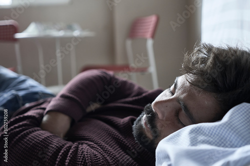 Handsome man sleeping in his bedroom. Man sleeping with alarm clock in foreground. Serene latin man sleeping peacefully.