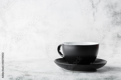 Black cup isolated on a white marble background. Horizontal photo. Tableware shop. Dishes shop. Advertising for dishware shop.