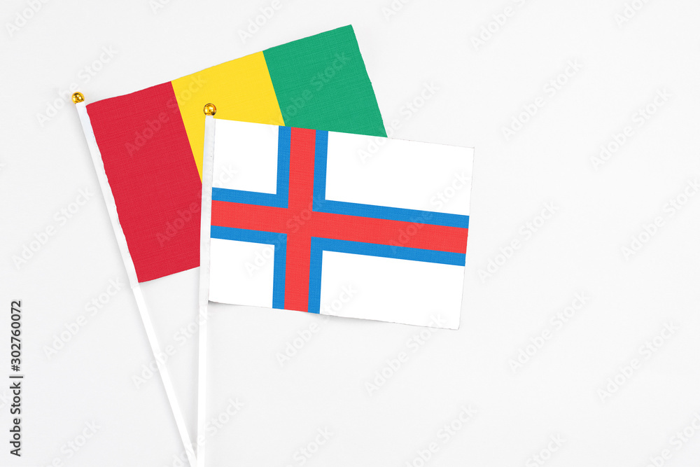 Faroe Islands and Guinea stick flags on white background. High quality fabric, miniature national flag. Peaceful global concept.White floor for copy space.