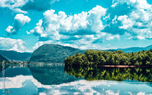 Scenery of Bohinj Lake, Slovenia. Nature in Slovenija. View of green forest and blue water. Beautiful landscape in summer. Alpine Travel destination. Julian Alps mountains on scenic background