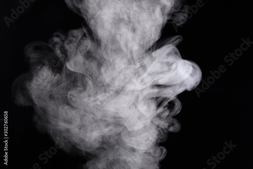 Puffs of white, gray smoke spread on a black background, curling in a fancy dance.