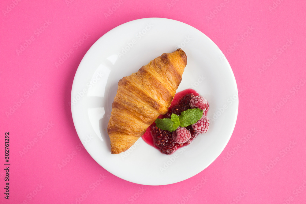 Croissant with raspberry jam in the white plate in the center of the pink background. Top view. Copy space. Croissant with raspberry jam in the white plate in the center of the pink background. Top view. Copy space.
