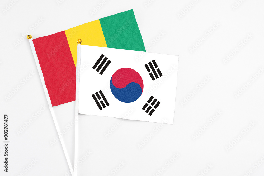 South Korea and Guinea stick flags on white background. High quality fabric, miniature national flag. Peaceful global concept.White floor for copy space.