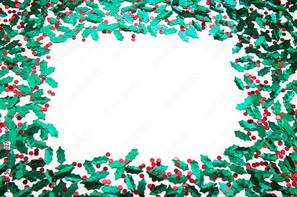Holiday frame of sprinkles of shiny green and red holly and berries confetti with blank white copy space
