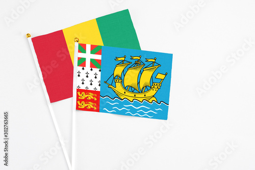 Saint Pierre And Miquelon and Guinea stick flags on white background. High quality fabric, miniature national flag. Peaceful global concept.White floor for copy space.