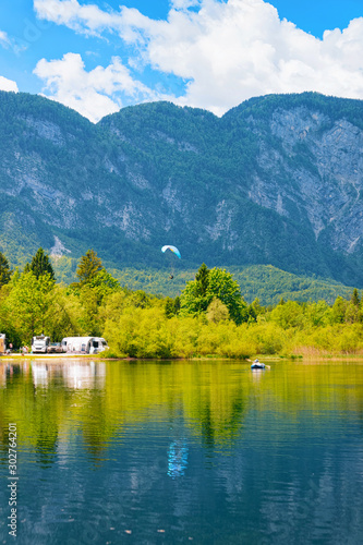 Scenery with camping of RV caravan trailers, people paragliding and canoe at Bohinj Lake in Slovenia. Nature and camper motorhomes in Slovenija. View of motor home van and mountains. Landscape
