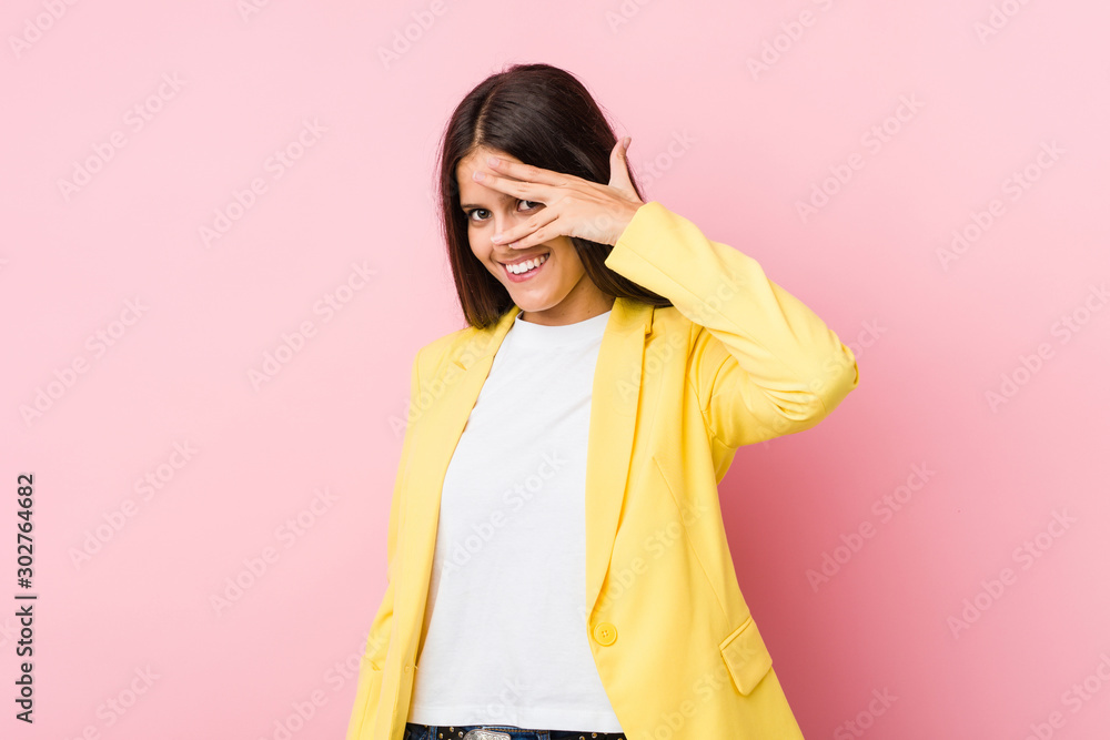 Fototapeta premium Young business woman blink at the camera through fingers, embarrassed covering face.