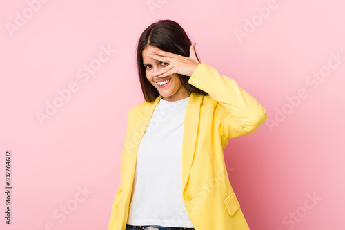Young business woman blink at the camera through fingers, embarrassed covering face. © Asier
