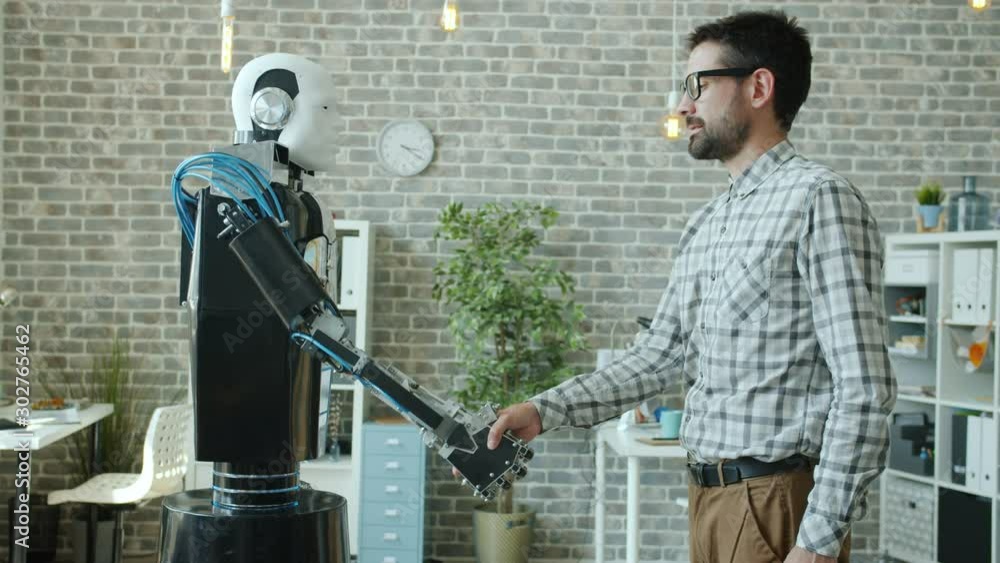 Young male developer and manlike robot cyborg are shaking hands ...