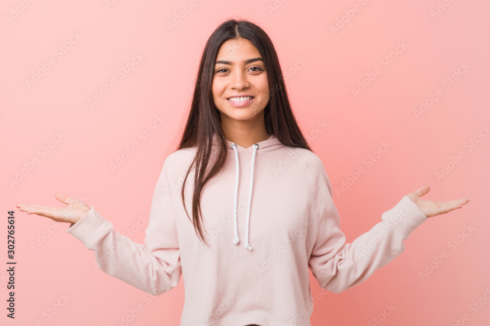 Young pretty arab woman wearing a casual sport look makes scale with arms, feels happy and confident. Young pretty arab woman wearing a casual sport look makes scale with arms, feels happy and confident.