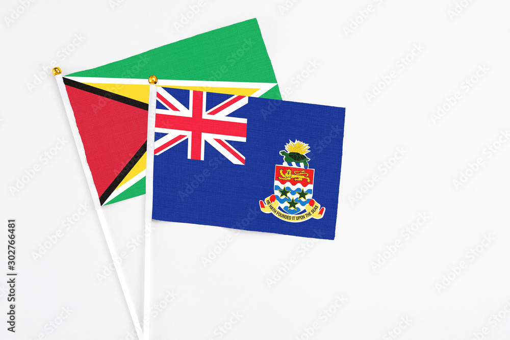 Fototapeta premium Cayman Islands and Guyana stick flags on white background. High quality fabric, miniature national flag. Peaceful global concept.White floor for copy space.